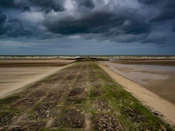 Road passing through land against cloudy sky