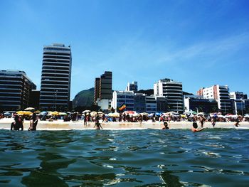 People enjoying at beach by city against sky