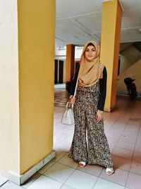 Portrait of smiling woman wearing hijab standing by column at basement