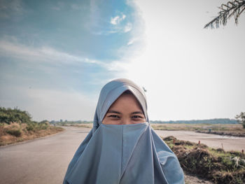 Portrait of young woman standing against sky