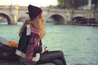 Woman sitting over river against bridge