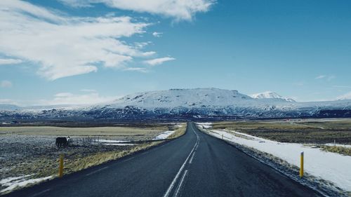 Road by snowcapped mountains against sky