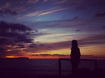 Rear view of silhouette woman standing at beach during sunset