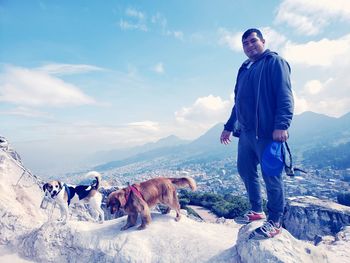 Full length of man with dogs on mountain peak against sky