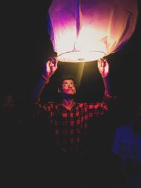 Portrait of young man holding illuminated lamp at night