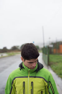 Man wearing green jacket standing on street against sky