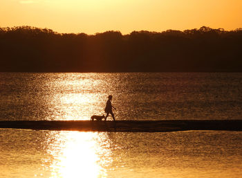 Silhouette man in sea against sky during sunset