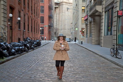 Full length portrait of smiling woman amidst buildings on street in city