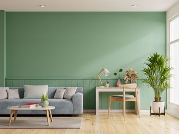 Interior mockup green wall with blue sofa and work table set in living room.3d rendering