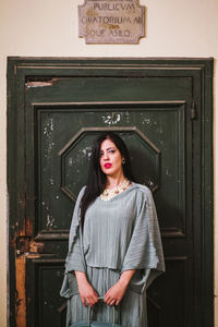 Portrait of young woman standing against closed door