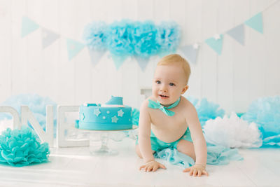 A one-year-old boy is on all fours against the background of a photo zone for his first birthday