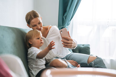 Young mother and cute baby girl using mobile phone at home