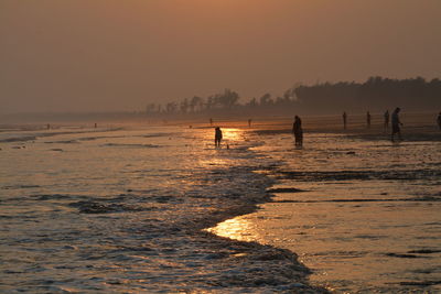 People at beach against sky during sunset