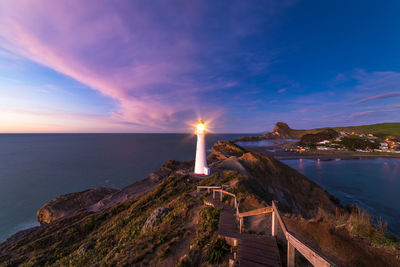 Lighthouse on mountain by sea against sky during sunset