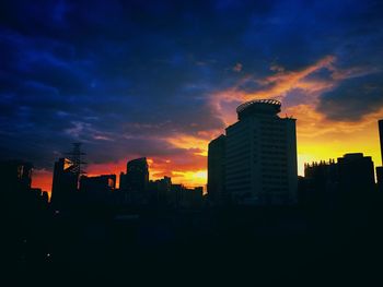 Silhouette of buildings against cloudy sky at dusk