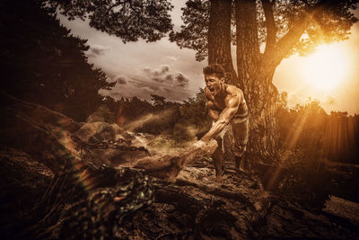 Man standing by tree in forest against sky at sunset