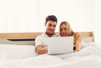 Smiling young woman using phone on bed at home