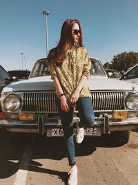 Young woman wearing sunglasses while sitting on car