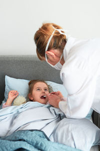 Female doctor examining girl lying on bed