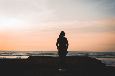 Rear view of silhouette woman standing at beach during sunset