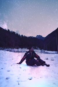 Man sitting on snow field against sky