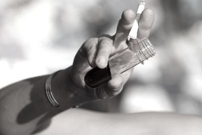 Cropped hand holding cigarette and liquid in bottle