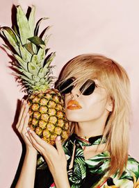 Close-up of young woman holding pineapple against colored background