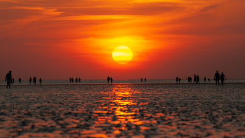 Silhouette people on beach against orange sky