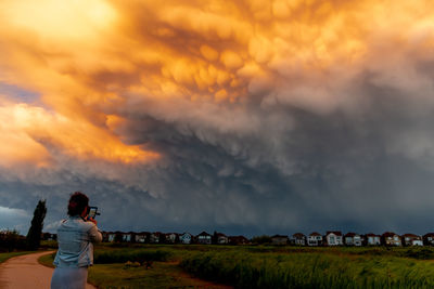 Side view of woman standing on field against sky during sunset