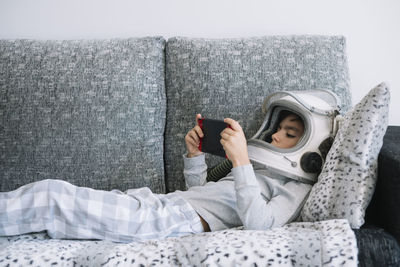 Adorable kid wearing pajama while sitting on couch. he is lying on couch while playing with a video game console at home