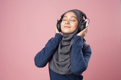 Young woman listening music against pink background