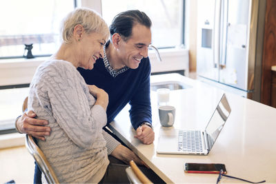 Smiling senior couple looking at laptop computer while sitting by table