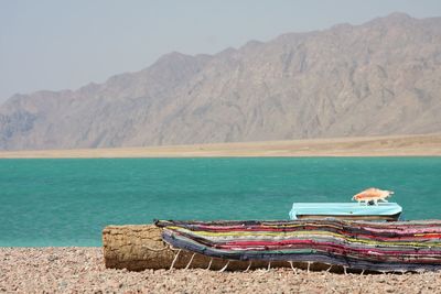 Deck chairs on shore by sea against mountains