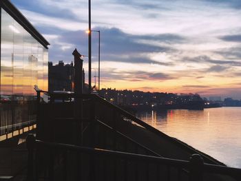 Silhouette city by river against sky during sunset