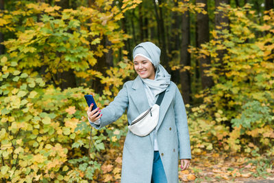 Portrait of smiling young woman standing in park during autumn