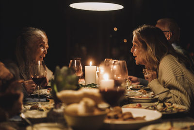 Senior woman talking to female friend at dining table during candlelight dinner party