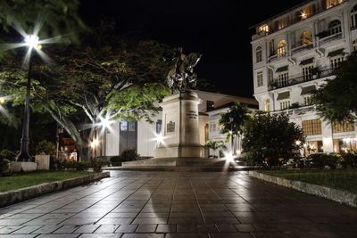 Illuminated street amidst buildings against sky at night