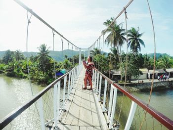 Rear view of people on footbridge against sky