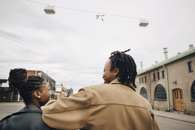 Rear view of smiling woman with friend walking on street in city