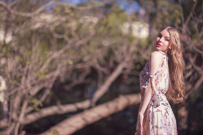 Beautiful young woman standing against trees in park