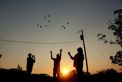 Silhouette people juggling balls against clear sky during sunset