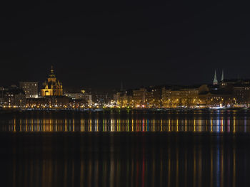 Illuminated buildings by river against sky at night