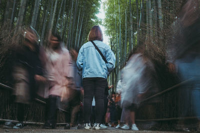 Rear view full length of woman standing on busy footpath in bamboo grove