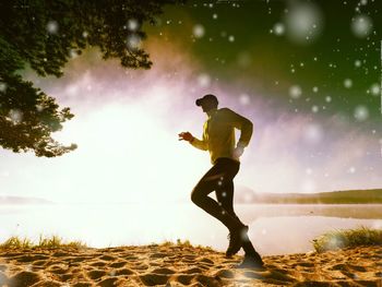 Freeze movement of running man on sandy beach at lake. shinning snowflakes agains sun.  light flare