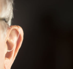 Cropped image of man with hearing aid against black background