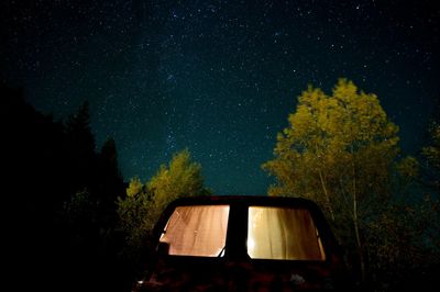 Illuminated motor home by trees against sky at night