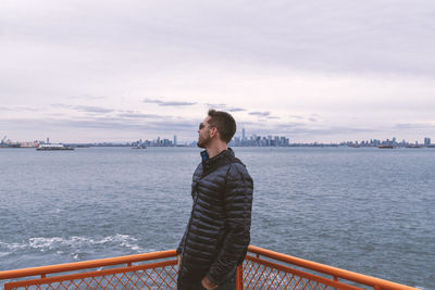 Man riding the staten island ferry gazing  wearing sunglasses and stylish puffer black winter coat.