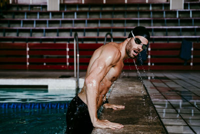 Shirtless young male swimmer leaning on poolside