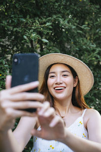 Smiling young woman doing selfie while standing against plants