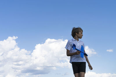 Low angle view of girl standing against blue sky